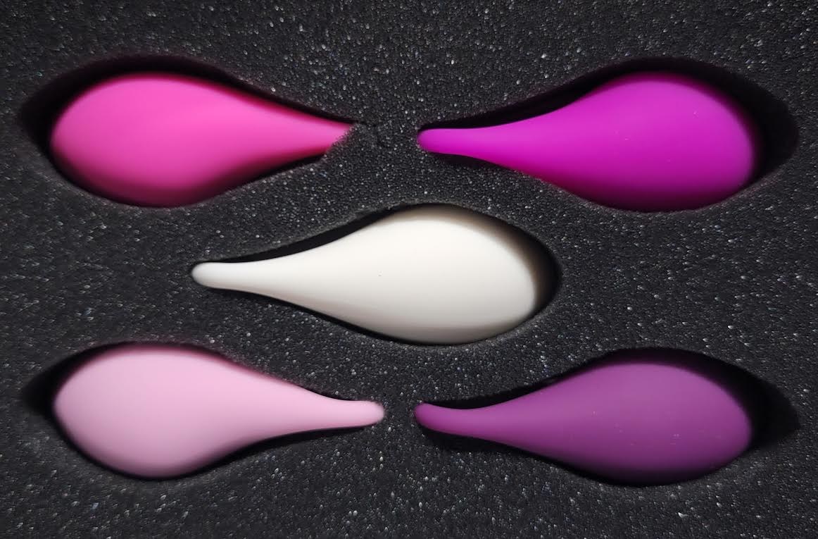 Actual five-piece exercise weight set in white, pink and purple, arranged in its foam case